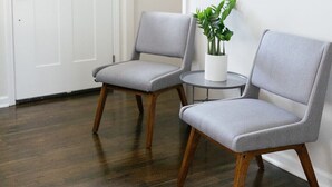 Une pièce comprenant deux fauteuils gris à revêtement en tissu et à pieds en bois, une petite table ronde sur laquelle est posée une plante en pot, et une porte blanche.