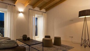 Un salon moderne avec un canapé, une table basse et une lampe. Il y a une grande fenêtre avec des rideaux, une porte donnant sur une autre pièce et un tapis à motifs sur le sol.