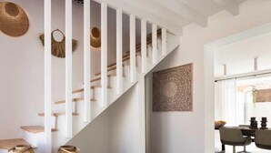 Un intérieur moderne avec un escalier blanc, des œuvres d’art décoratives au mur et un coin repas comprenant des chaises et une table.