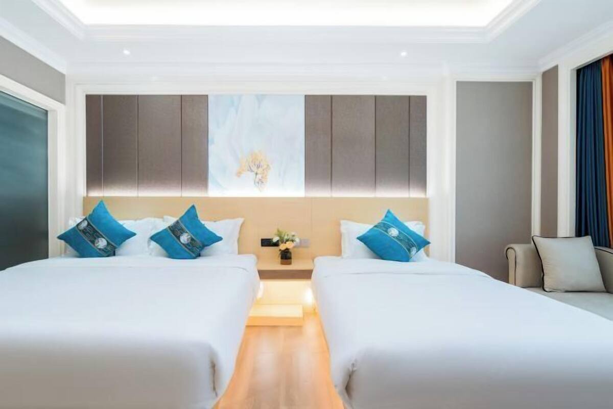 Quarto de hotel com duas camas, uma mesa de cabeceira central, uma obra de arte na parede e vista para a cidade.