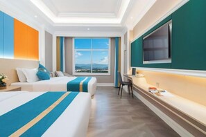 A hotel room with two beds, a desk, a chair, a TV, and a large window with a view. - Junyuan Hotel (Mangshi)