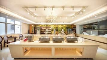 A hotel kitchen with a central island, overhead lighting, and a view of the dining area.