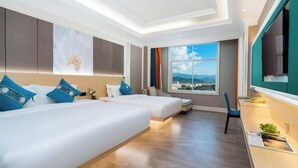 Habitación de hotel con dos camas, un escritorio, un ventanal grande con vistas a la ciudad y un televisor montado.