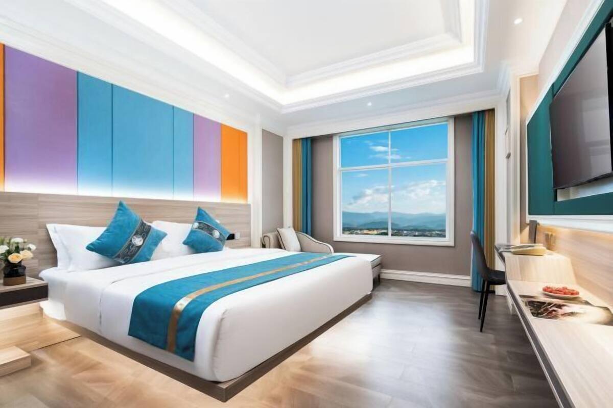 Quarto de hotel moderno com uma cama grande, uma mesa de escritório, uma televisão e uma janela com vista.