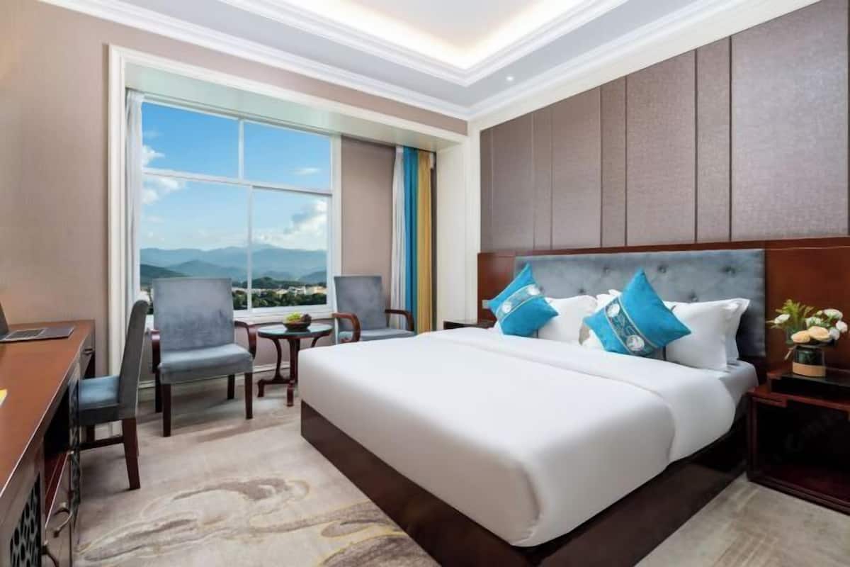 Quarto de hotel com uma cama grande, uma escrivaninha, uma cadeira e vista para as montanhas.