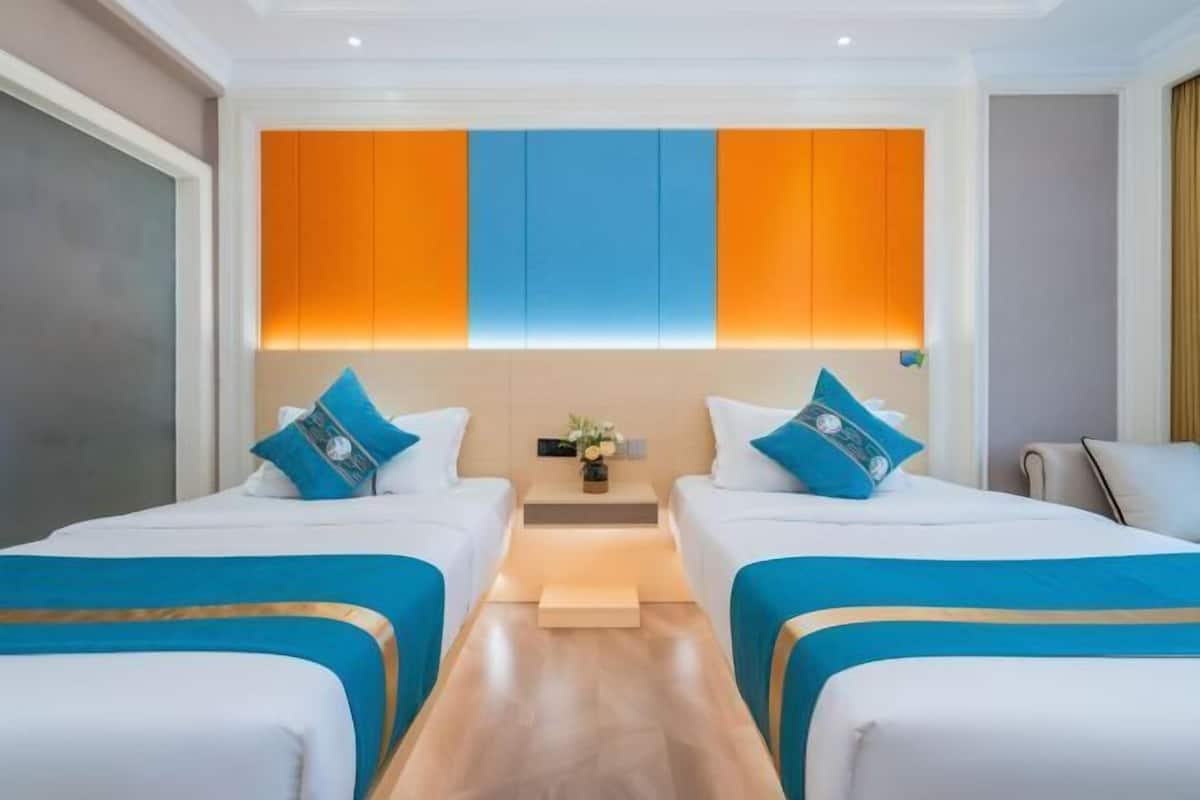 Quarto de hotel com duas camas, uma mesinha de cabeceira e um painel na parede com seções laranja e azul.