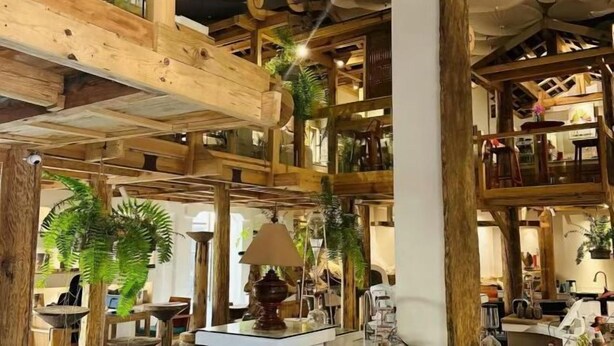 Interior de madera con varios niveles, vigas a la vista, una columna central y diferentes muebles.