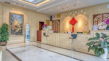A hotel lobby with a reception desk, seating area, and a large painting on the wall.