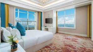 Habitación de hotel con cama, escritorio, televisión y ventanas amplias con vistas.