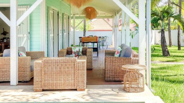 A covered outdoor seating area with wicker furniture, a pool, and a view of a house in the background.