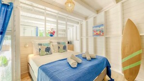 A bedroom with a bed, pillows, a surfboard, and a window with curtains.