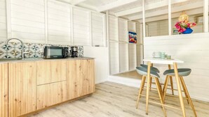 A modern kitchen with a wooden countertop, a microwave, and a coffee maker. There is a white dining area with two chairs and a table.