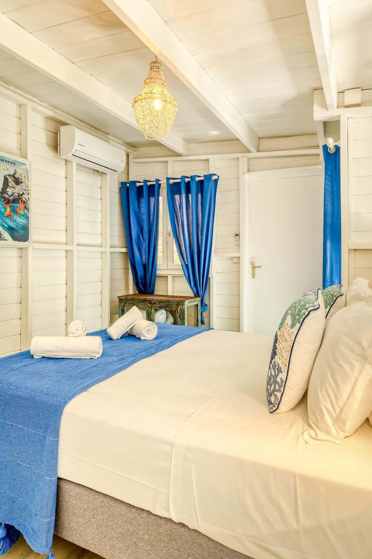 Un dormitorio con una cama, cortinas azules, una mesita con toallas y un cartel en la pared.