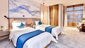 Habitación de hotel con dos camas, un cuadro abstracto grande, un área de comedor y vistas a través de amplios ventanales.