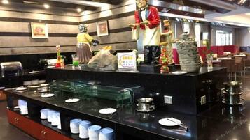 Zona de bufé con dispensadores de comida, platos y una estatua.