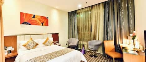 A hotel room with a bed, a desk, a chair, a nightstand, a painting, and a large window with curtains.