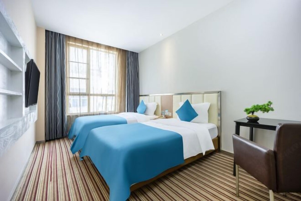 A hotel room with two beds, a TV, a desk, and a chair.