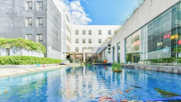 A swimming pool with koi fish, surrounded by modern buildings with large windows and a clear sky. - Shanshui Trends Hotel (Guangzhou Huangpu East Road Dasha East Subway Station) (Guangzhou)