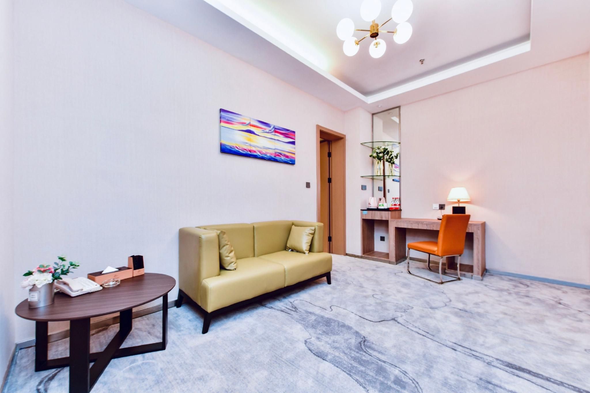 Una habitación de hotel moderna con un sofá, un escritorio, una silla, una mesa redonda y un cuadro en la pared.