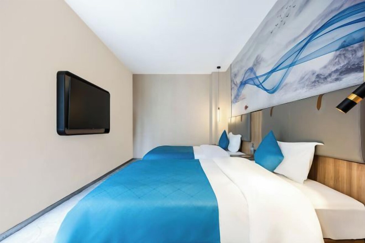 A hotel room with a bed, a flat-screen TV mounted on the wall, and a large abstract painting above the bed.