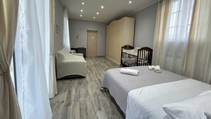 Quarto de hotel com duas camas, um berço, um guarda-roupa e uma escrivaninha.
