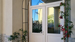 Uma porta branca com um painel de vidro, ladeada por plantas em vasos, e um arco de metal acima.