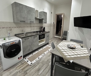 A compact kitchen with a built-in washer, oven, and sink, a dining area with a checkered tablecloth, and a flat-screen TV.