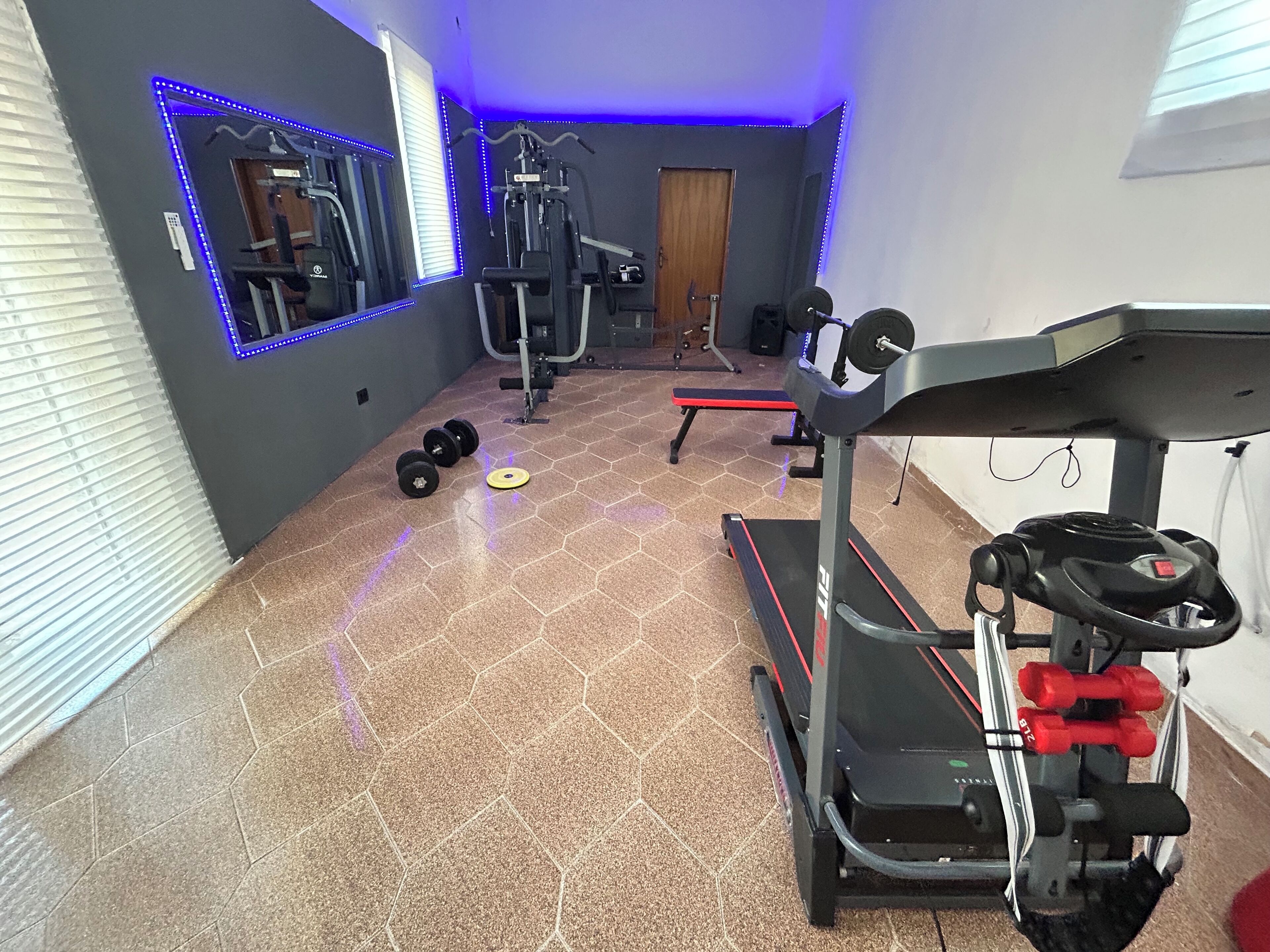 Een fitnessruimte met trainingsapparatuur, een loopband en een spiegelwand.