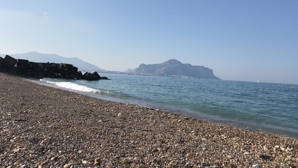 Uma praia de pedras com águas calmas e montanhas ao longe.