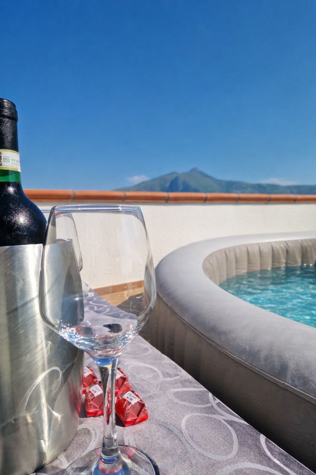 Eine Weinflasche und ein Glas auf einem Balkon mit Pool und Bergblick.
