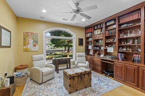 A living room with a large bookshelf, two armchairs, a coffee table, and a view of a garden through a window. - A True Gem | Spacious Backyard (St. George)