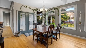Une salle à manger avec une table et des chaises en bois, un lustre et une vue sur l’extérieur grâce à de grandes fenêtres.