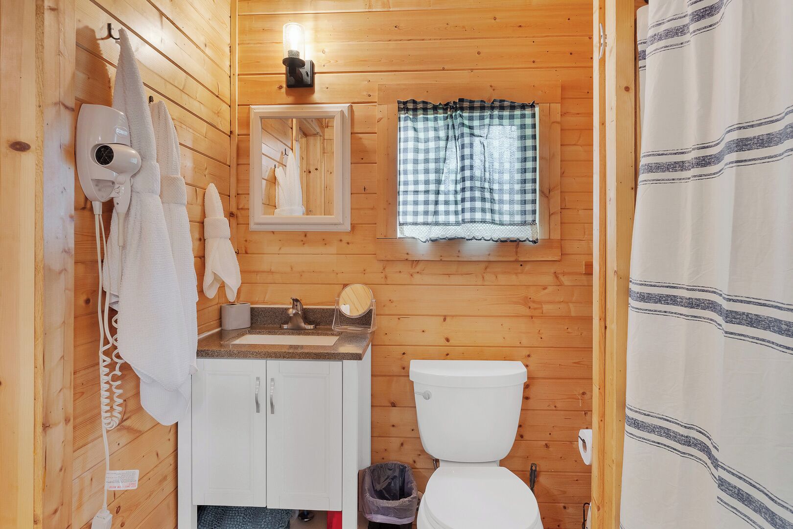 Une salle de bain rustique, aménagée dans une cabane en bois, avec un lavabo, des toilettes et un porte-serviettes.