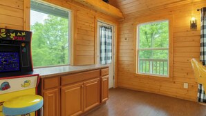 Interior de una cabaña de madera con cocina, ventanas amplias y una pequeña barra.