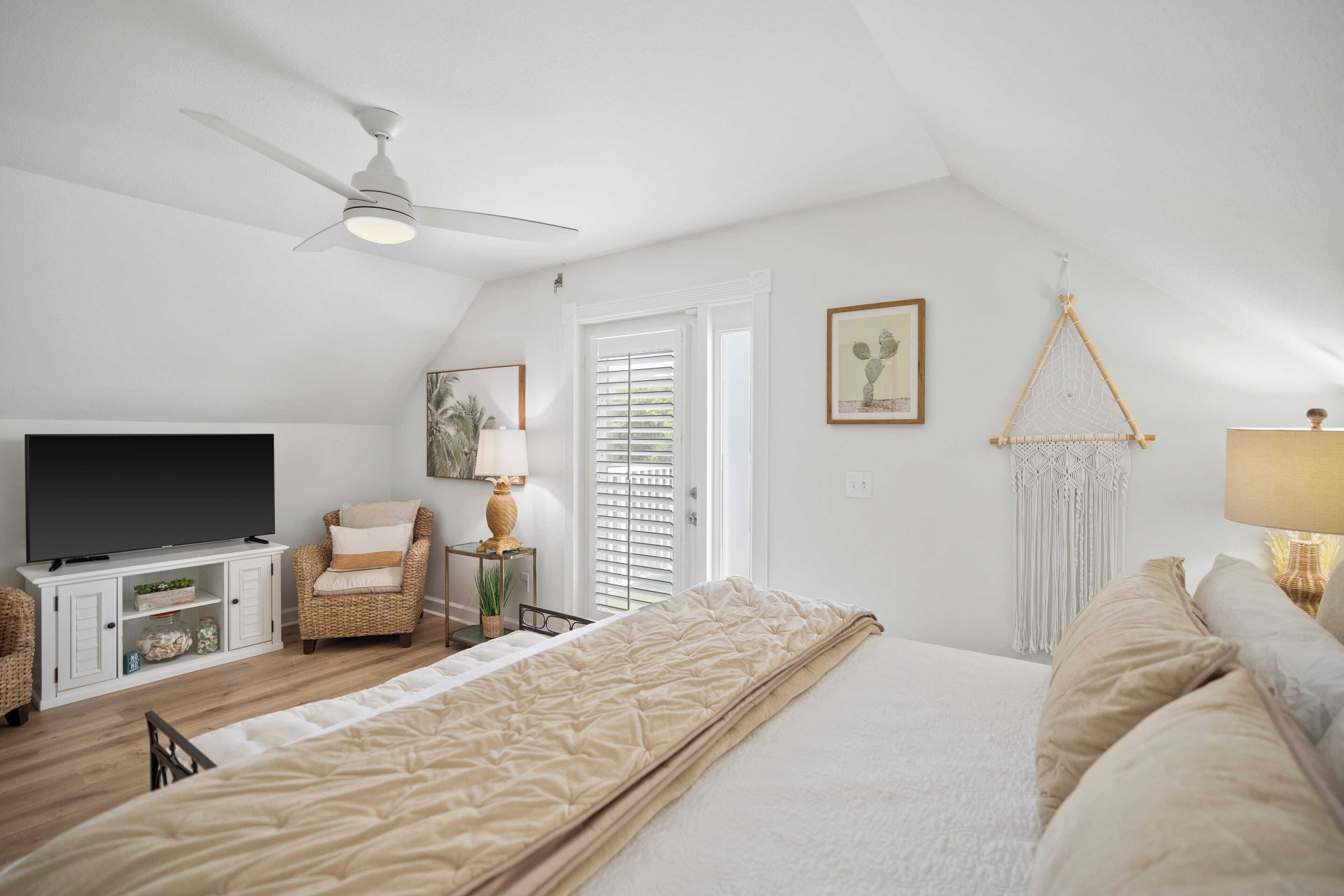 Ein Schlafzimmer mit Bett, Fernseher, Sessel, Schreibtisch und Deckenventilator.