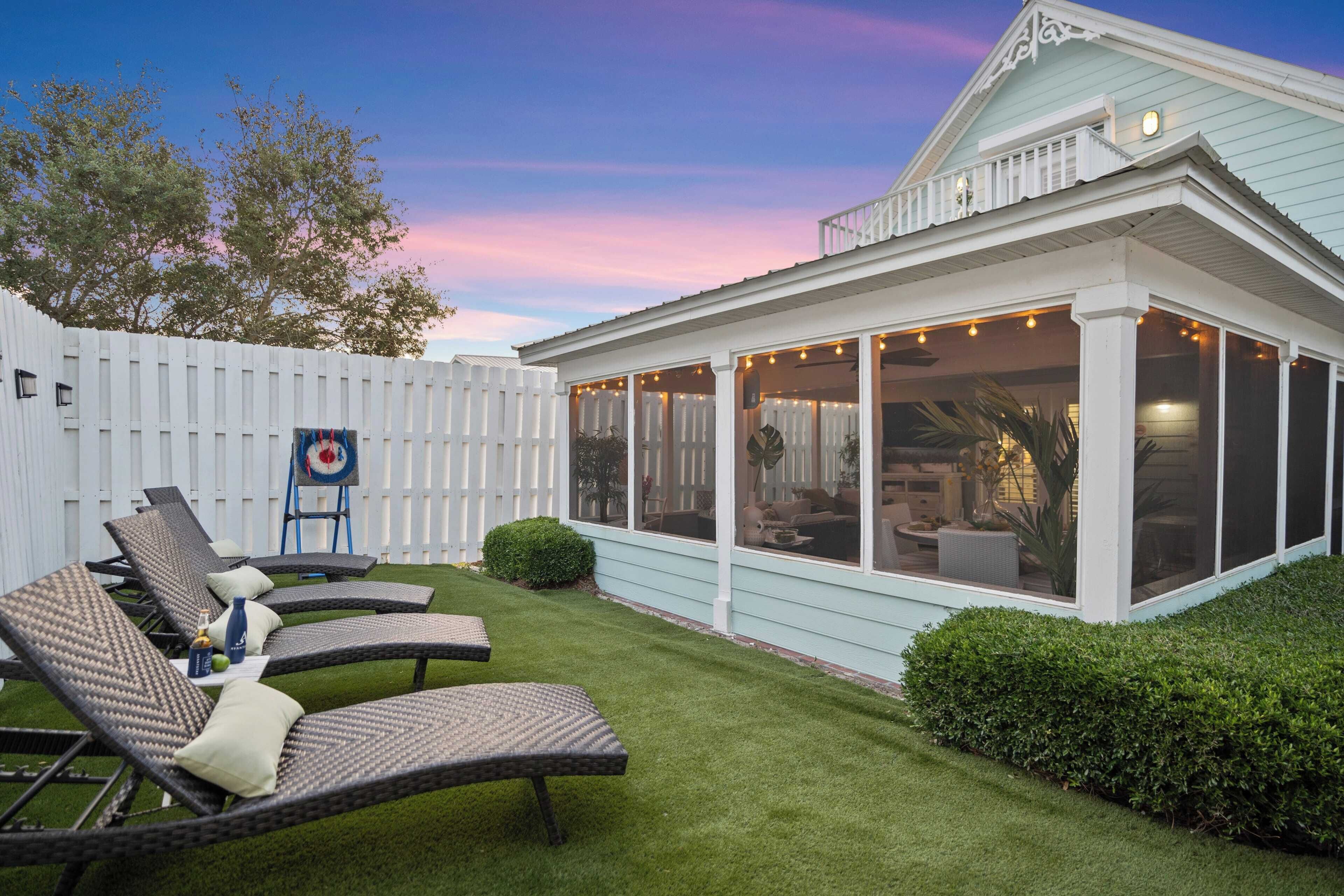 A covered patio with wicker furniture and a white fence.
