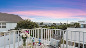 A balcony with a white railing, a table with a vase of flowers, a bottle of water, and a glass of wine. - Newly Renovated! 2-min Walk to the Beach The Coastal Cottage by Avantstay (Panama City Beach)