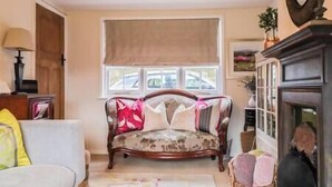 A living room with a sofa, a lamp, a cabinet, and a window with blinds. - Beautiful 2 Bedroom Period Cottage (Rivenhall)