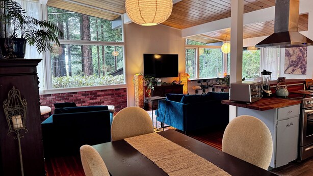 Een moderne keuken met een groot eiland, houten plafond en grote ramen met uitzicht op het bos.