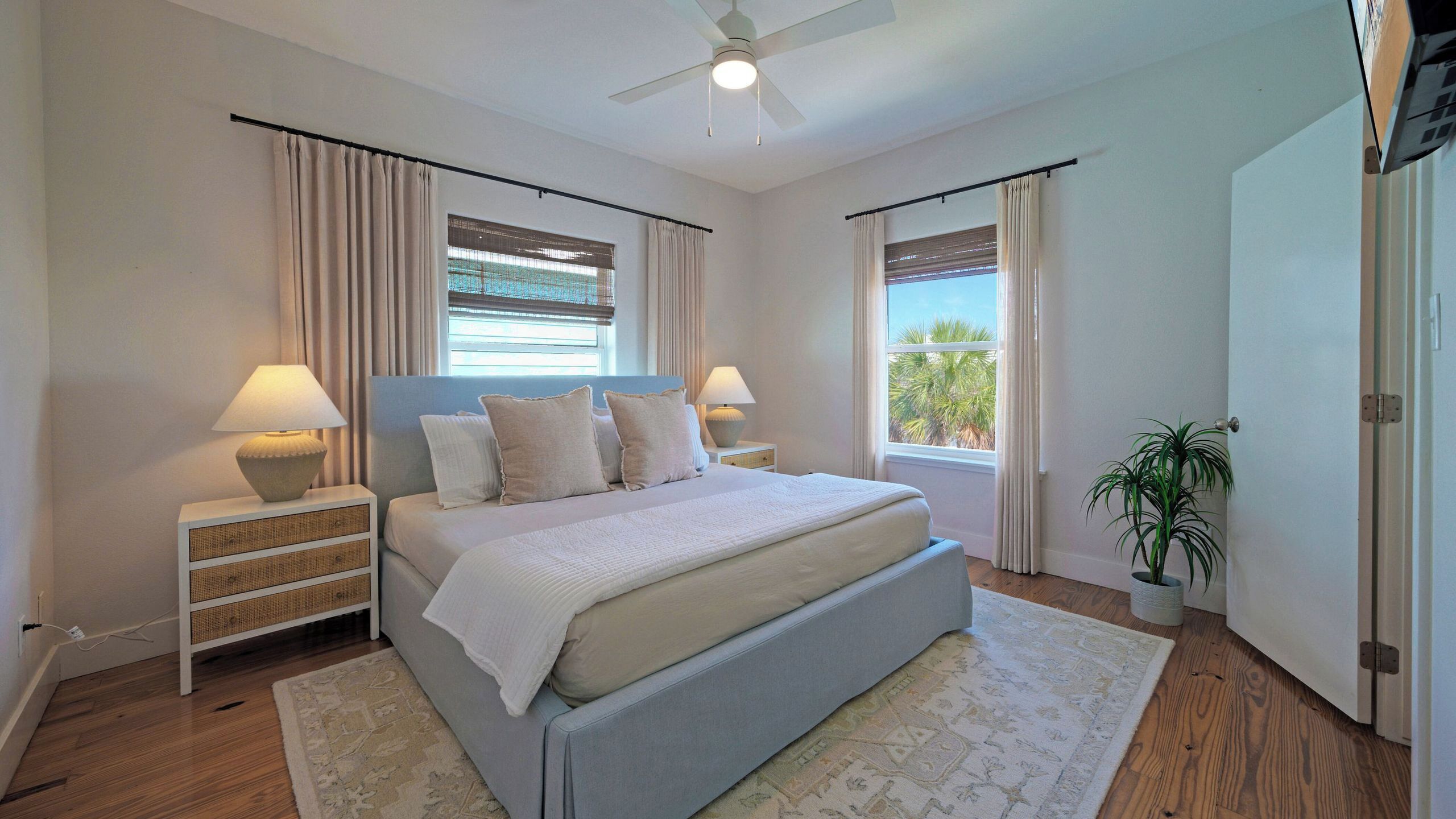 A bedroom with a bed, two bedside tables, a ceiling fan, and a window with curtains.