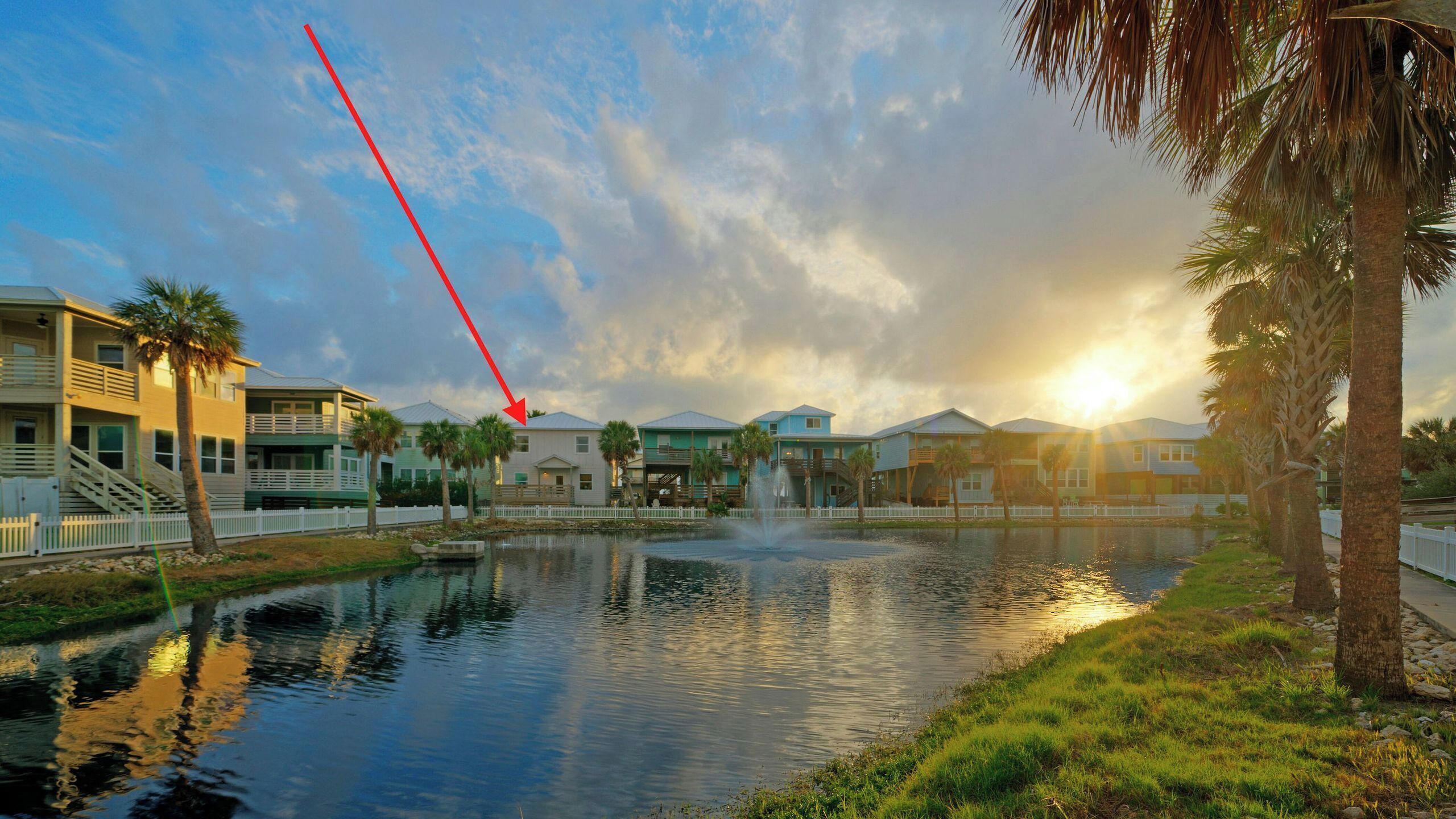 A waterfront property with a pond, a white fence, and a row of buildings with balconies.