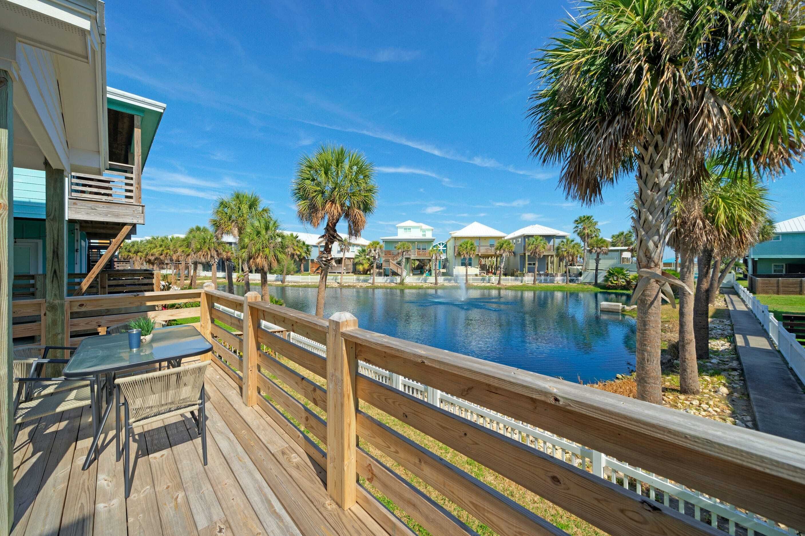 A wooden deck with a pool, palm trees, and a view of other buildings.