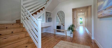 Un pasillo amplio con suelo de madera, una escalera blanca y un banco.