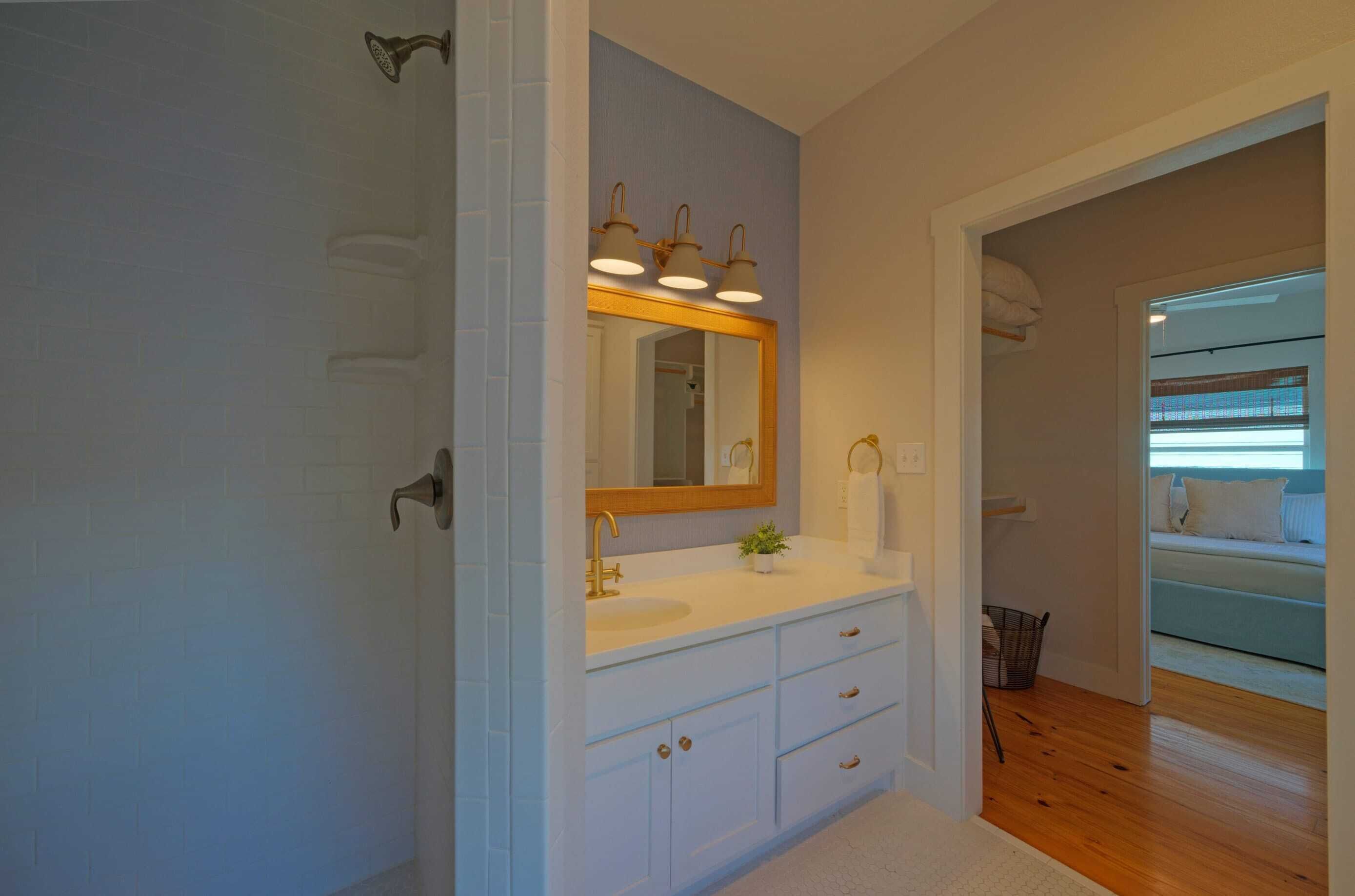 A bathroom with a white vanity, a mirror with three lights, and a wooden floor.