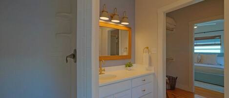A bathroom with a white vanity, a mirror with three lights, and a wooden floor.