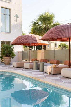 A poolside area with checkered umbrellas, cushioned seating, and a potted plant. - Charleston Stay | 2 Queen Beds + Wellness Perks (Charleston)