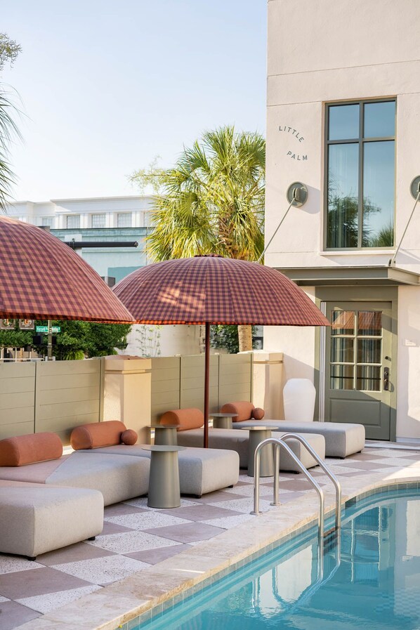 A poolside area with checkered umbrellas, cushioned seating, and a pool. - Charleston Stay | 2 Queen Beds + Wellness Perks (Charleston)