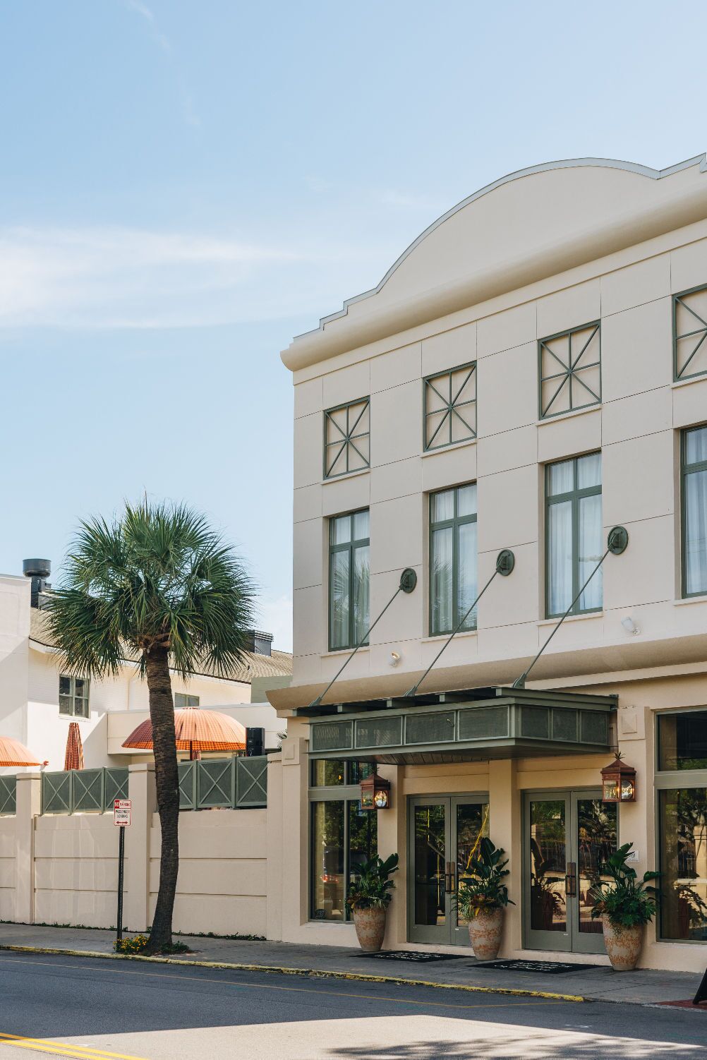 A building with a flat facade, large windows, and a covered entrance area with potted plants.