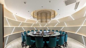 Ein moderner Konferenzraum mit einem runden Tisch, blaugrünen Stühlen und geometrischer Beleuchtung.