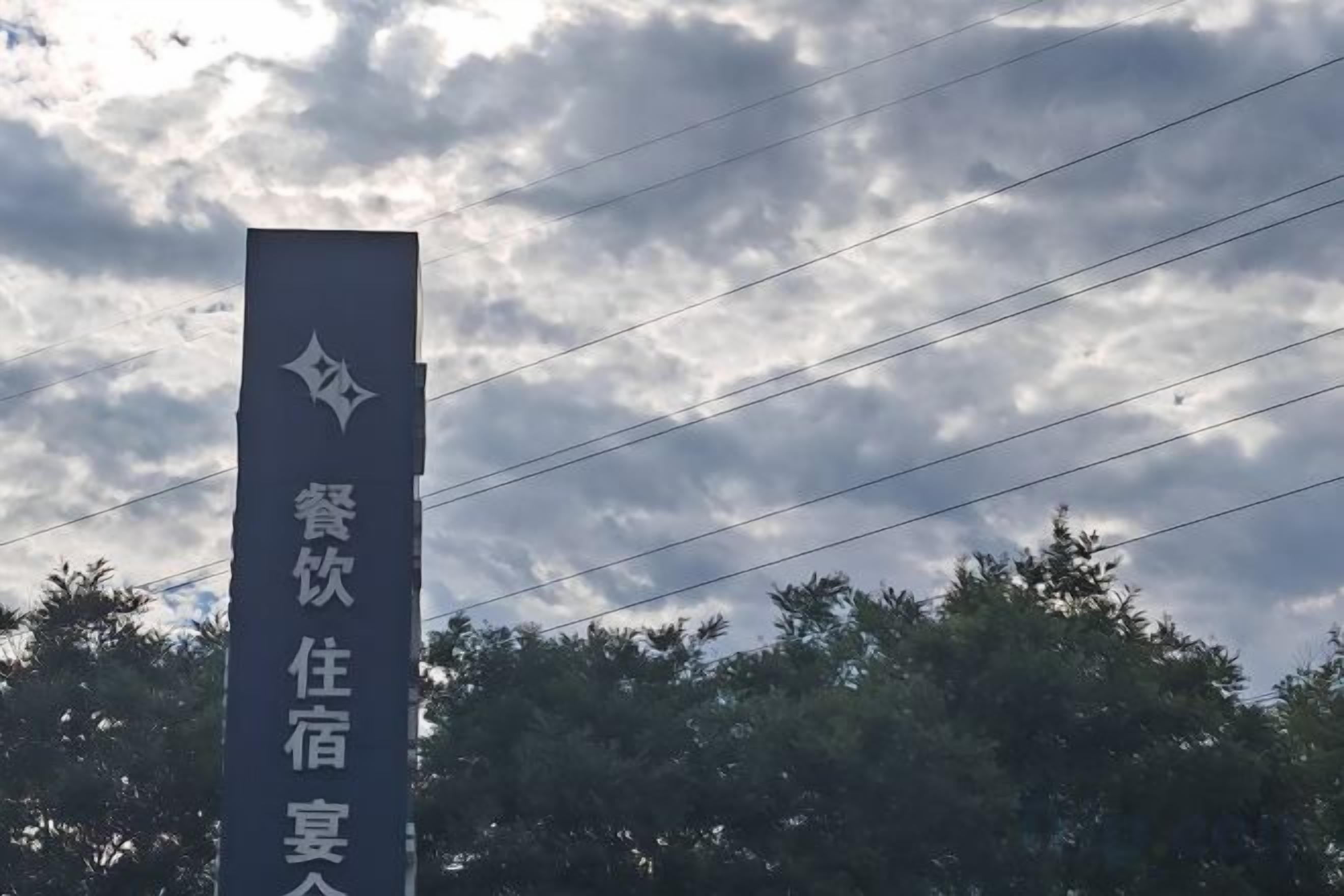 A vertical sign with text against a cloudy sky.